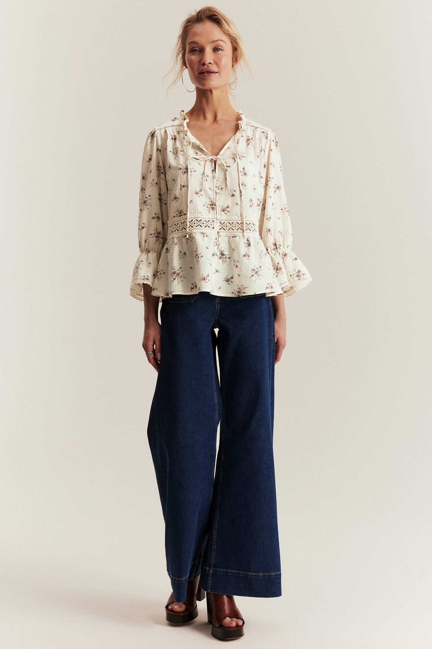 Woman wearing a floral blouse and blue pants on a plain background