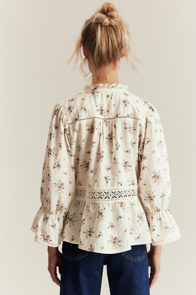 Woman wearing a floral blouse with long sleeves against a plain background