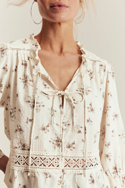 Floral blouse with lace details worn by a person on a light background