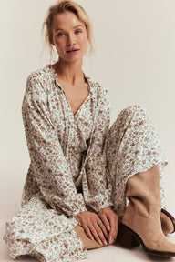 Woman wearing a floral dress and beige boots sitting on the floor against a plain background